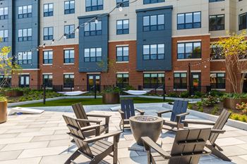 An outdoor patio with chairs and a fire pit in front of an apartment building